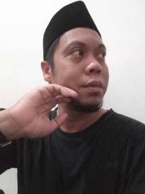 Foto Ihsan Ariswanto mengenakan kaos hitam, tersenyum, dan memakai songkok hitam